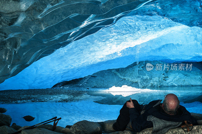 在北欧滑雪后，老人在岩石上休息，到达尼加兹布林冰川内的这个令人惊叹的蓝色冰洞，这是Jostedalsbreen最容易接近的手臂，Europeâ大陆上最大的冰川，在冬天的一天，它在春天融化